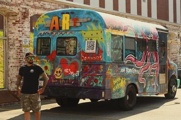 Man standing in front of an artfully painted school bus.